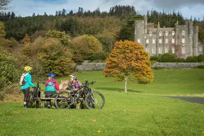 Mountain bikers resting in Castlewellan Forest Park, with Castlewellan Castle behind them